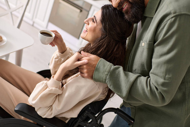 καλλιεργημένη άποψη χαρούμενης ανάπηρου γυναίκας σε αναπηρική καρέκλα πίνοντας καφέ με τον σύζυγό της στο πρωινό - Φωτογραφία, εικόνα
