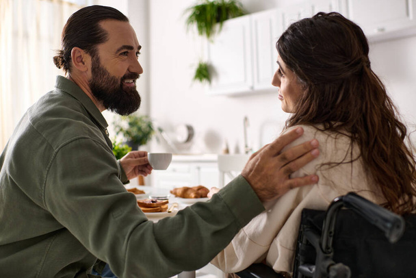 przystojny wesoły człowiek korzystających śniadanie z jego niepełnosprawny wesoły żona na wózku inwalidzkim na śniadanie - Zdjęcie, obraz