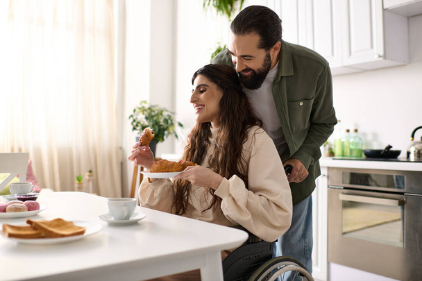 cheerful man having great time at breakfast with his beautiful disabled wife that eating croissant - Photo, Image