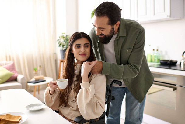 бородатий люблячий чоловік обіймає свою інвалідну гарну дружину під час сніданку на кухні вдома - Фото, зображення