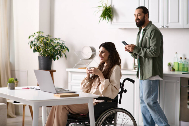 pretty disabled woman in wheelchair working remotely near her husband looking at phone on backdrop - Photo, Image