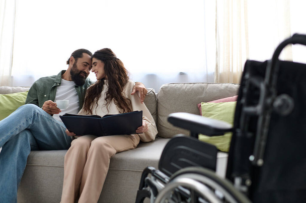radosny brodaty mężczyzna spędza czas na laptopie ze swoją niepełnosprawną piękną żoną, pijąc kawę - Zdjęcie, obraz