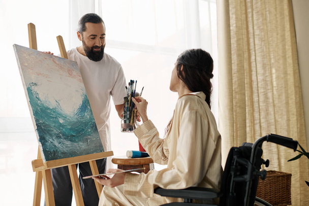 loving cheerful couple of bearded man and disabled woman painting on easel together at home - Photo, Image