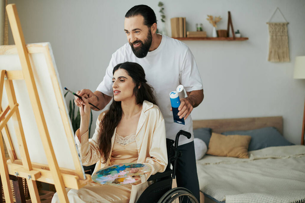 premuroso marito jolly aiutando la sua moglie inclusiva di bell'aspetto a dipingere sul cavalletto mentre a casa - Foto, immagini