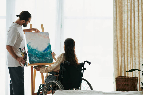 自宅で一緒にイーゼルに絵を描く魅力的な陽気な男と障害のある女性のカップル - 写真・画像