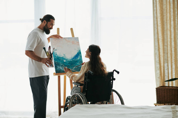 ελκυστικό χαρούμενο ζευγάρι γενειοφόρος άνδρας και ανάπηρη γυναίκα ζωγραφική στο καβαλέτο μαζί στο σπίτι - Φωτογραφία, εικόνα