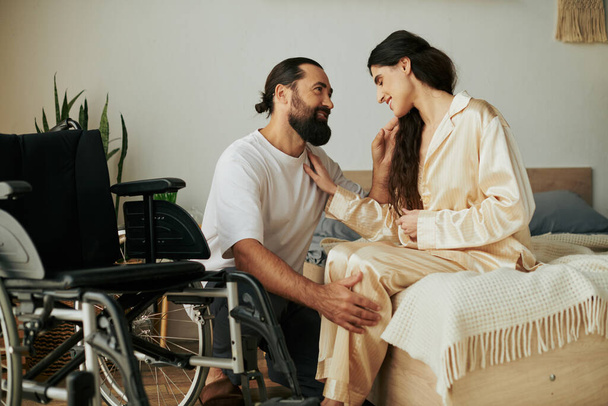 бородатий люблячий чоловік в домашньому вбранні допомагає своїй інвалідній дружині переодягнутися в піжаму в спальні вдома - Фото, зображення