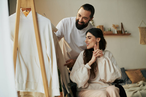 szakállas gondoskodó férfi segít inkluzív felesége tolószék öltözni, míg a hálószobában - Fotó, kép