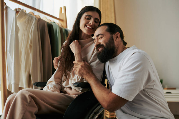 ελκυστικός χαρούμενος άντρας που περνάει χρόνο με την όμορφη ανάπηρη γυναίκα του ενώ είναι στο υπνοδωμάτιο στο σπίτι - Φωτογραφία, εικόνα