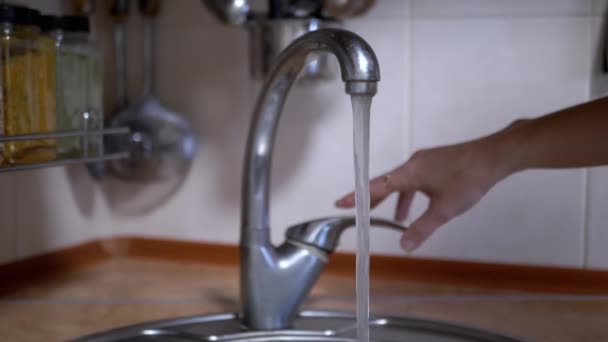 La main ouvre le robinet avec de l'eau courante dans la cuisine sur fond flou. Ferme là. L'eau propre et transparente s'écoule dans l'évier. Au ralenti. Consommation, économie des ressources naturelles en eau à la maison. - Séquence, vidéo