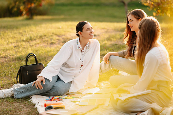 Jonge vrouwelijke studenten hebben plezier tijdens het zitten en studeren op een deken in het park. - Foto, afbeelding