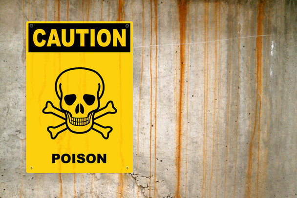 Gele waarschuwingsbordje geschroefd aan een betonnen muur om te waarschuwen voor een bedreiging. In het midden van het paneel, is er een schedel & kruisbeenderen symbool en de boodschap is: "Voorzichtig, Poison". - Foto, afbeelding