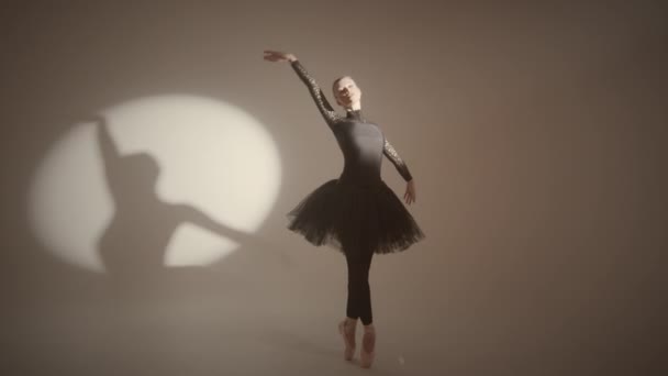 Full shot of graceful ballerina in black tutu dancing classical ballet on pointe under spotlight in studio with cyc wall - Footage, Video