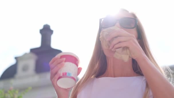 Eine junge Frau isst vor dem Hintergrund der Sonnenstrahlen ein Croissant. Das Frühstückskonzept auf der Straße. Traditionelles französisches Frühstück - Filmmaterial, Video