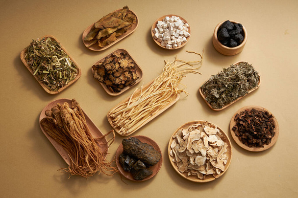 Medicina tradicional china con hierbas colocadas en placas de madera sobre fondo marrón claro. Vista superior, escena para publicidad de medicina - Foto, Imagen
