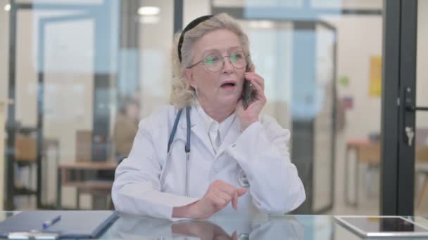 Vanhempi naislääkäri puhuu puhelimessa potilaan kanssa - Materiaali, video