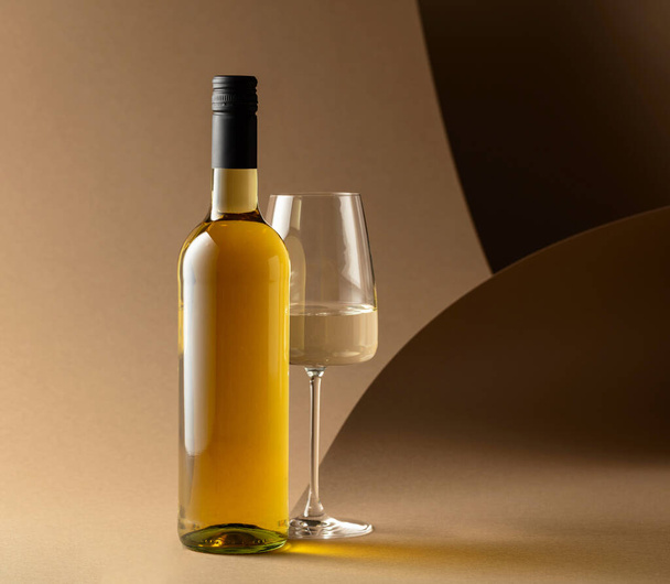 Bottiglia e bicchiere di vino bianco su sfondo beige. - Foto, immagini
