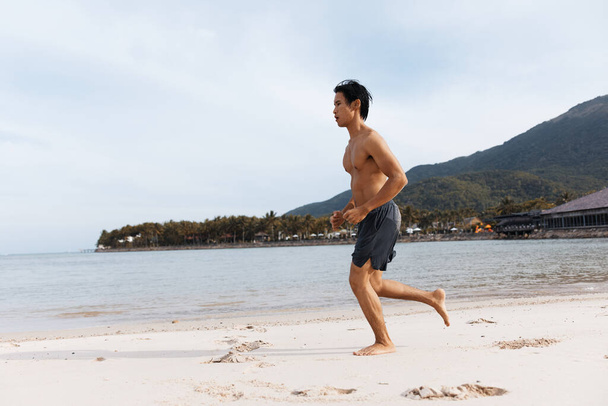 Спортсмен азіатський чоловік обіймає свободу і здоров'я під час бігу на пляжі на заході сонця - Фото, зображення