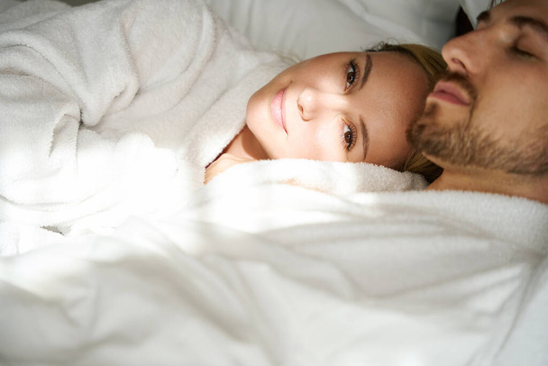 Glückliche junge Frau döst auf der Schulter ihres geliebten Mannes, Paar entspannt auf einem großen Bett - Foto, Bild