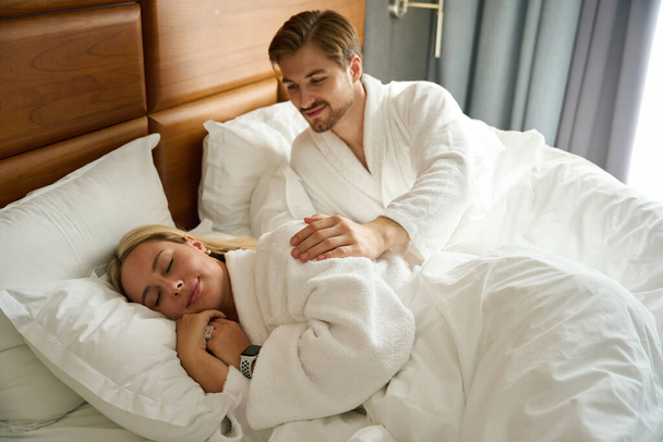 Genç adam tatlı sarışın bir kadınla uyanır, bir çift büyük bir yatakta dinlenir. - Fotoğraf, Görsel