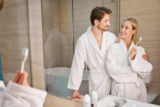 Cara com uma namorada na casa de banho fazendo sua rotina matinal, um casal em roupões terry aconchegante - Foto, Imagem