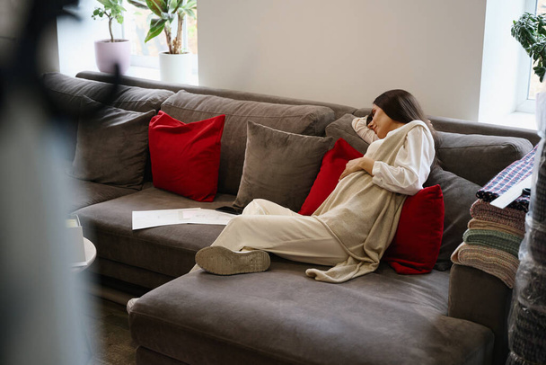 Moe zwangere vrouw is doezelen op zachte kussens in de ontspanningsruimte, naast haar zijn werken schetsen van kleding - Foto, afbeelding