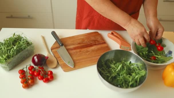 Mulher preparando delicioso e saudável almoço em casa cozinha. Close up tiro de mãos femininas cortando um tomate cereja fresco com faca na tábua de madeira.  - Filmagem, Vídeo