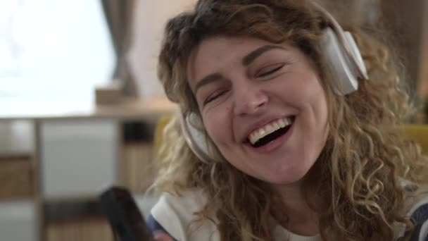 Een blanke vrouw volwassen vrouw met koptelefoon gebruik maken van mobiele telefoon thuis om te luisteren naar de muziek online vrolijke glimlach zing vreugde veel plezier alleen kopieer ruimte - Video