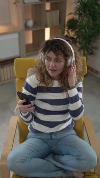 Jedna kaukaska kobieta dorosła kobieta ze słuchawkami używa telefonu komórkowego w domu, aby słuchać muzyki online szczęśliwy uśmiech śpiewać radość bawić się sam kopiować przestrzeń - Materiał filmowy, wideo