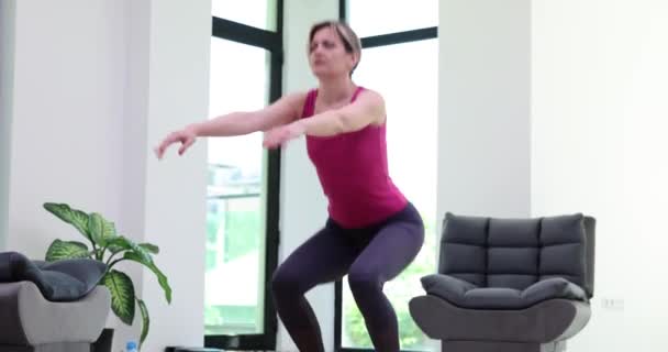 Mulher atlética fazendo agachamento e parar de se exercitar sentindo dor aguda no joelho durante o treino de fitness em casa. Esportista tocando perna na lesão e aptidão - Filmagem, Vídeo