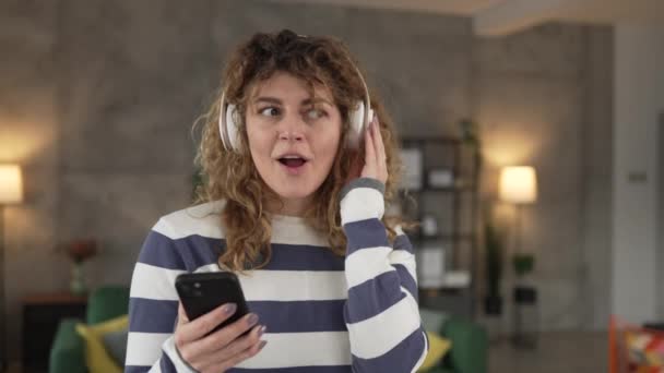ヘッドフォンを持つ1人の白人女性大人の女性は,音楽を聞くために自宅で携帯電話を使用する オンライン幸せな笑顔歌の喜びは,単独のコピースペースを持っています - 映像、動画