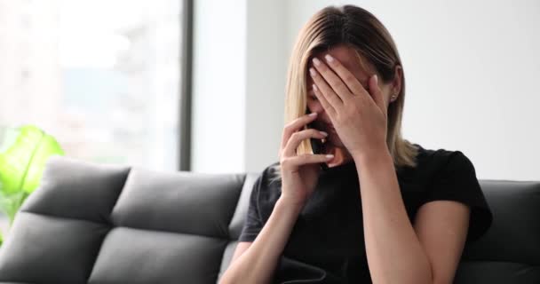 Stressed woman sitting on sofa in living room talking on smartphone worried and listening to bad news. Woman feels desperate and unpleasant remote conversation, - Footage, Video