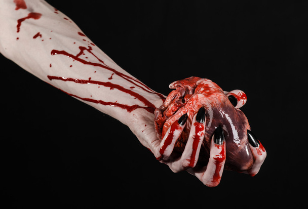 Bloody horror and Halloween theme: Terrible bloody hands with black nails holding a bloody human heart on a black background isolated background in studio - 写真・画像