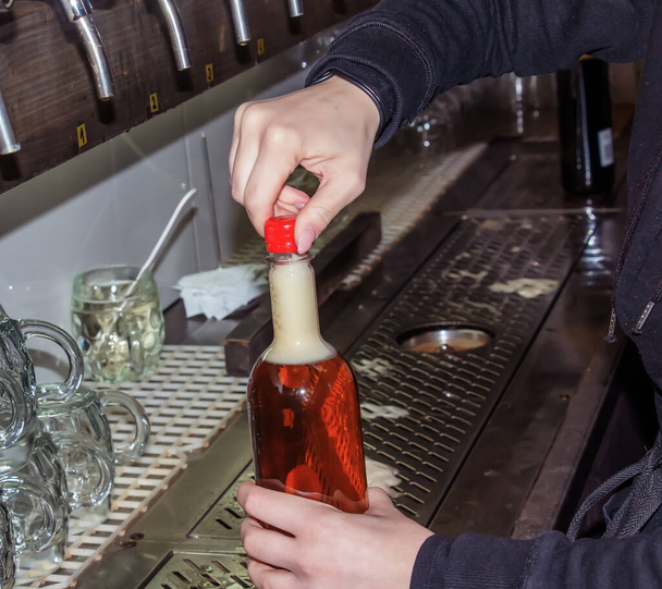 Behind the counter. Women's hands beautifully and easily pour beer into a bottle. - Photo, Image