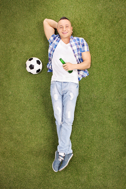 Young football fan lying on grass - Zdjęcie, obraz
