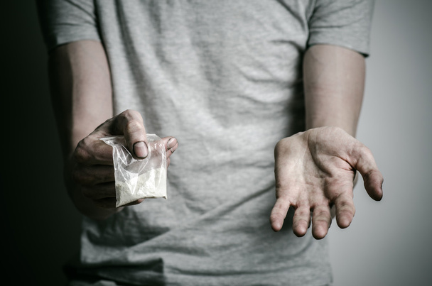 The fight against drugs and drug addiction topic: addict holding package of cocaine in a gray T-shirt on a dark background in the studio - Fotoğraf, Görsel