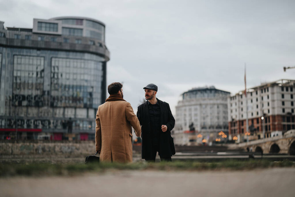 Casual zakelijke ontmoeting van twee goed geklede mannen die een boeiende discussie met een modern stadsgezicht op de achtergrond. - Foto, afbeelding