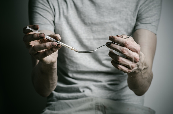 The fight against drugs and drug addiction topic: addict holding spoon lighter and heats the liquid drug in a T-shirt on a dark background - Foto, afbeelding