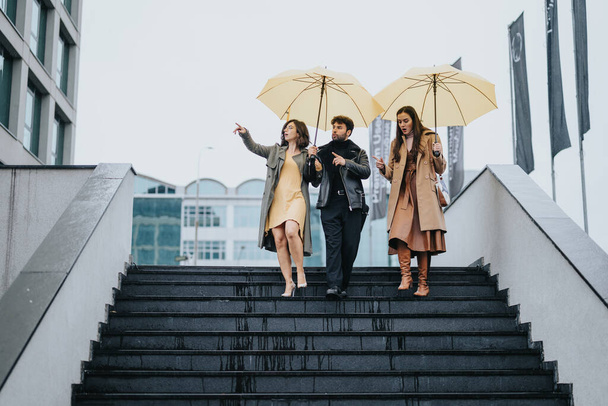 雨の街の階段に傘を持った3人のビジネス同僚. - 写真・画像