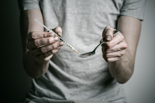 The fight against drugs and drug addiction topic: addict holding spoon lighter and heats the liquid drug in a T-shirt on a dark background - Foto, imagen