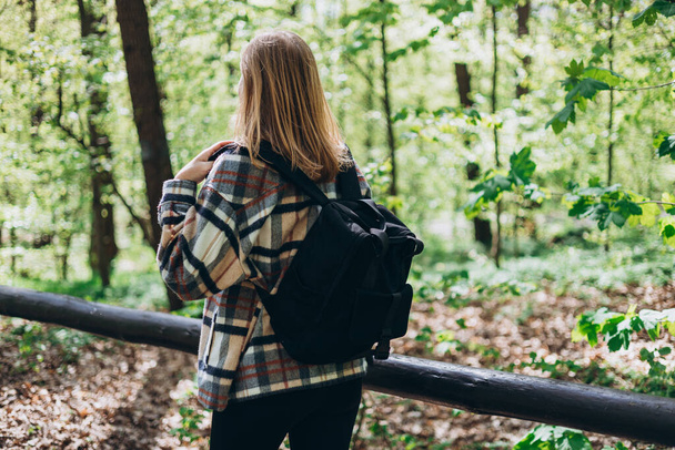 Vista trasera de la mujer joven con traje casual, lleva una mochila negra caminando por el bosque. Primavera. 30s Mujeres en ropa deportiva senderismo en el bosque - Foto, Imagen