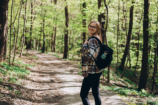 Fiatal nő alkalmi ruhában, fekete hátizsákot visel az erdőben sétálva. Tavasz van. 30-as évek Nők sport ruhák túrázás az erdőben - Fotó, kép