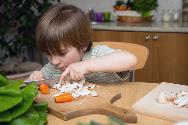 Left-Handed Boy Cutting Carrot on a Wooden Board Very Carefully in the Kitchen - 写真・画像