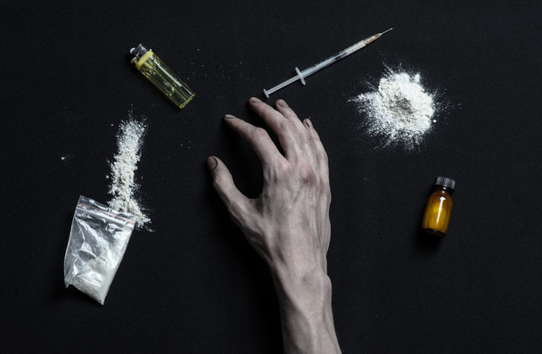The fight against drugs and drug addiction topic: hand addict lies on a dark table and around it are drugs, a top studio - Photo, image