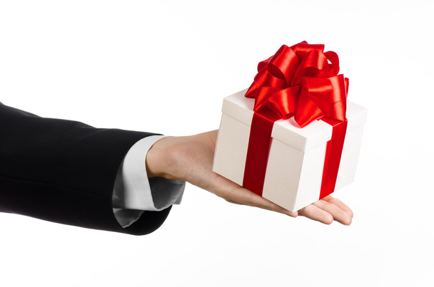 El tema de las celebraciones y regalos: un hombre en un traje negro con un regalo exclusivo envuelto en una caja blanca con cinta roja y lazo, el regalo más hermoso aislado sobre fondo blanco en el estudio
 - Foto, Imagen