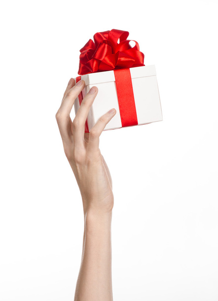 Juhlien ja lahjojen teema: käsi, jolla on valkoiseen laatikkoon kääritty lahja, jossa on punainen nauha ja jousi, kaunein lahja, joka on eristetty valkoisella taustalla studiossa.
 - Valokuva, kuva