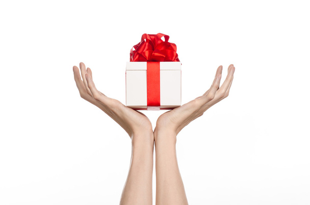 El tema de las celebraciones y regalos: la mano sosteniendo un regalo envuelto en caja blanca con cinta roja y lazo, el regalo más hermoso aislado sobre fondo blanco en el estudio
 - Foto, Imagen