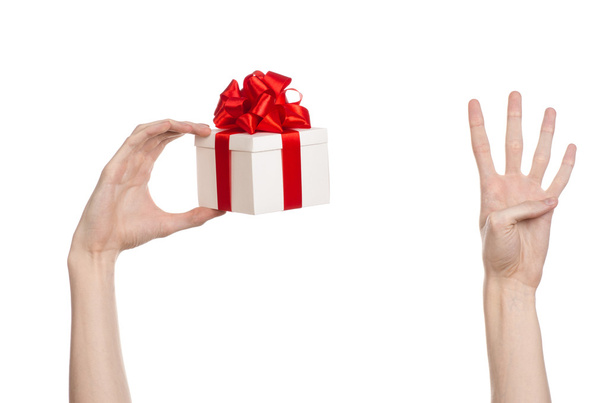 Тема святкування та подарунків: рука тримає подарунок, загорнутий у білу коробку з червоною стрічкою та бантом, найкрасивіший подарунок ізольований на білому тлі в студії
 - Фото, зображення