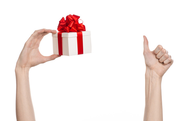 A téma az ünnepségek és ajándékok: kezében egy ajándék csomagolva fehér doboz piros szalag és az íj, a legszebb ajándék elszigetelt fehér background stúdióban - Fotó, kép