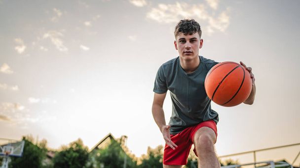Een tiener Kaukasische mannelijke Kaukasische jongeman staan op basketbalveld met bal in de avond klaar om spel kopiëren ruimte echte persoon spelen - Foto, afbeelding